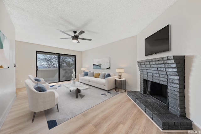 living room featuring ceiling fan, a fireplace, a textured ceiling, and light wood-type flooring