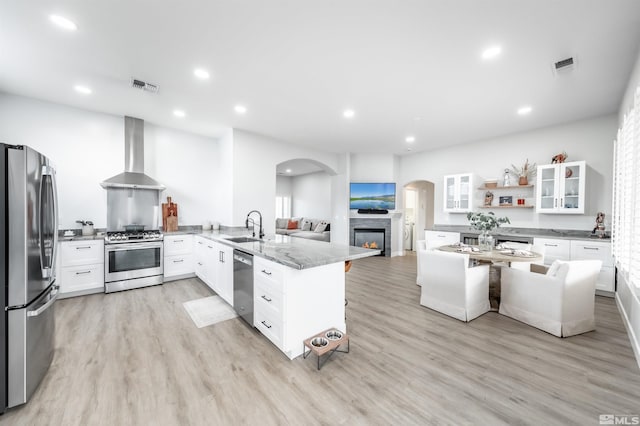 kitchen with wall chimney range hood, sink, appliances with stainless steel finishes, white cabinetry, and light stone countertops