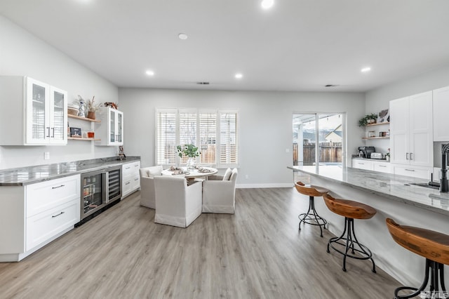 kitchen with white cabinetry, a kitchen bar, light stone counters, and light hardwood / wood-style floors