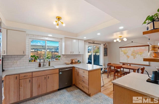 kitchen featuring sink, tasteful backsplash, a raised ceiling, stainless steel dishwasher, and kitchen peninsula