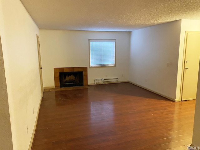 unfurnished living room featuring a baseboard heating unit, hardwood / wood-style floors, a tile fireplace, and a textured ceiling