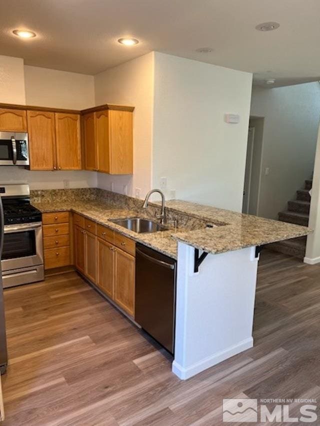 kitchen with a kitchen bar, sink, kitchen peninsula, stainless steel appliances, and light stone countertops