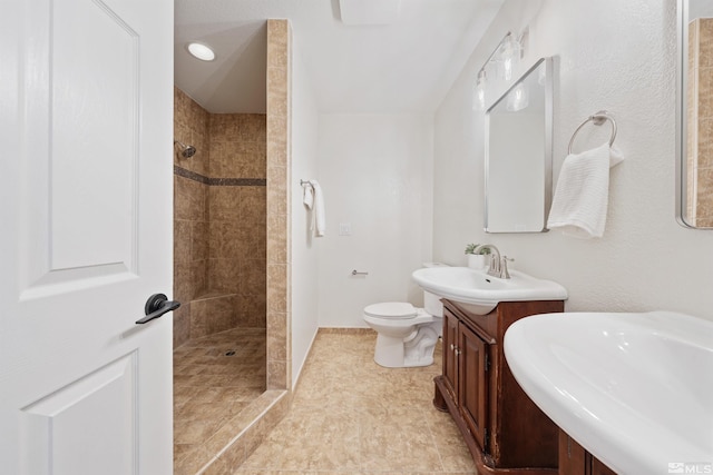 bathroom featuring a tile shower, vanity, and toilet