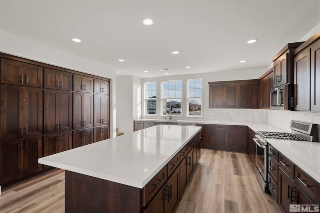 kitchen with backsplash, a center island, stainless steel appliances, dark brown cabinets, and light hardwood / wood-style flooring