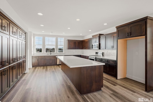 kitchen with dark brown cabinetry, sink, light hardwood / wood-style flooring, a kitchen island, and stainless steel appliances