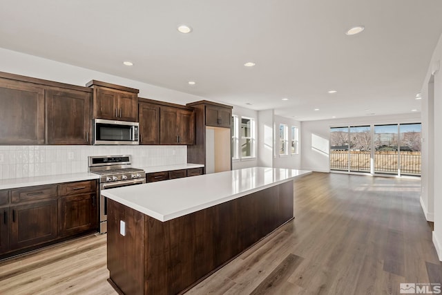 kitchen featuring dark brown cabinets, light wood-type flooring, a kitchen island, stainless steel appliances, and backsplash