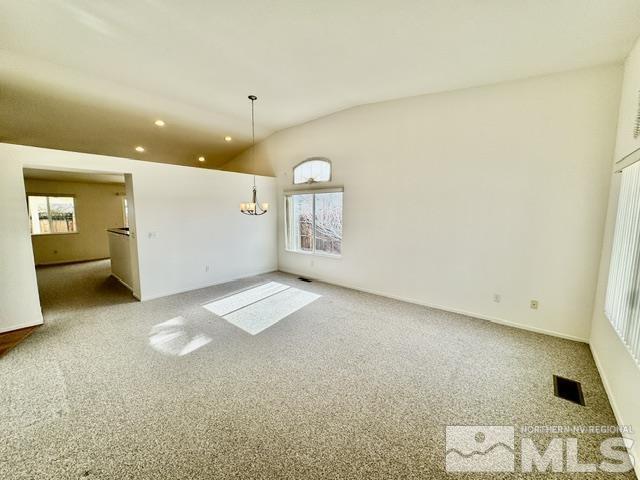 carpeted empty room featuring an inviting chandelier and lofted ceiling