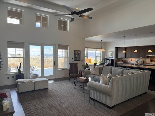 living room with dark wood-type flooring, ceiling fan, and a high ceiling