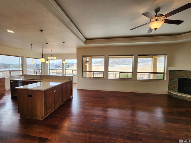 kitchen featuring decorative light fixtures, dark hardwood / wood-style floors, a raised ceiling, a fireplace, and a kitchen island with sink