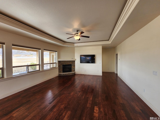 unfurnished living room with ceiling fan, ornamental molding, dark hardwood / wood-style flooring, a stone fireplace, and a raised ceiling