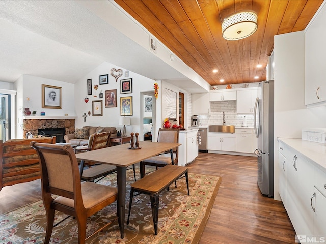 dining area with vaulted ceiling, a fireplace, sink, hardwood / wood-style flooring, and wood ceiling