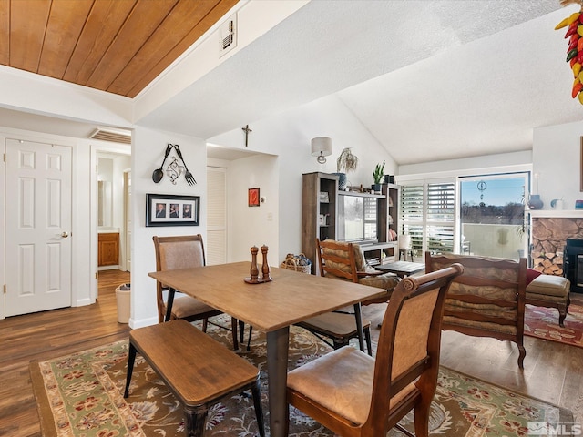 dining room with wood ceiling, dark hardwood / wood-style flooring, vaulted ceiling, and a stone fireplace