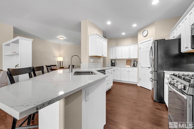 kitchen with a breakfast bar, sink, gas stove, light stone countertops, and white cabinets