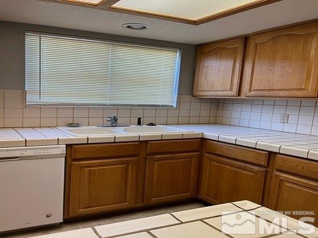 kitchen with tasteful backsplash, tile counters, dishwasher, and sink