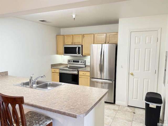 kitchen featuring a kitchen bar, sink, light brown cabinets, appliances with stainless steel finishes, and kitchen peninsula