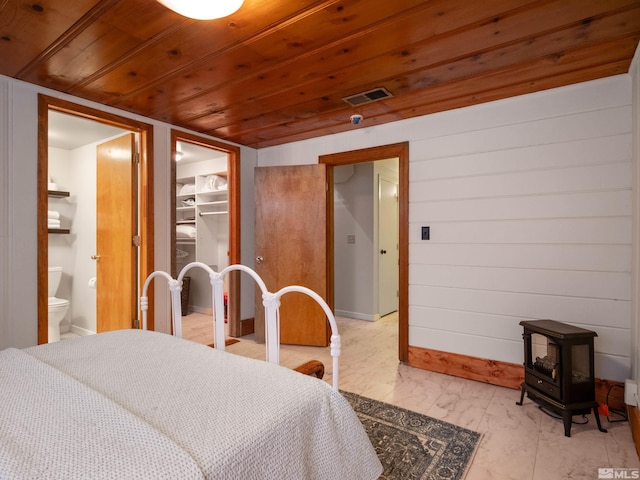 bedroom with ensuite bathroom, a spacious closet, a wood stove, wooden ceiling, and a closet