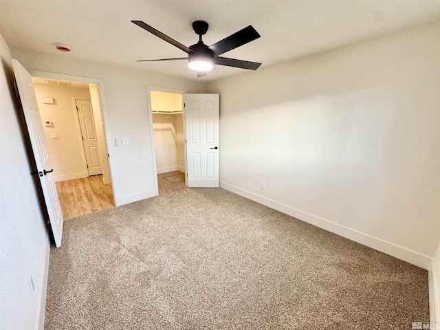 unfurnished bedroom featuring a walk in closet, light colored carpet, ceiling fan, and a closet