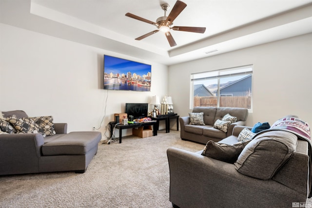 carpeted living room with ceiling fan and a raised ceiling