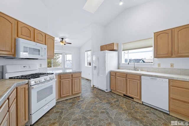 kitchen featuring a skylight, tile countertops, stone finish floor, a sink, and white appliances