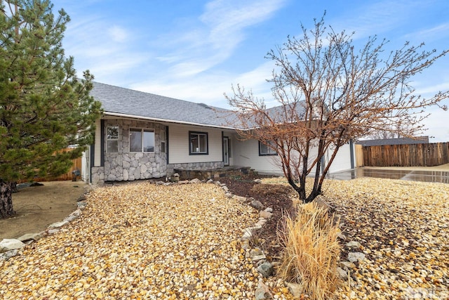 ranch-style house with stone siding, roof with shingles, an attached garage, and fence