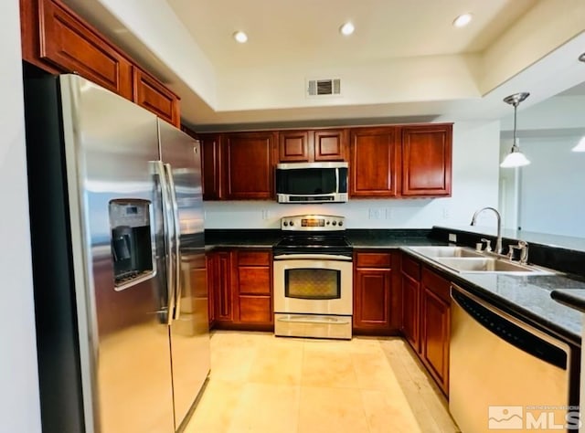 kitchen with a tray ceiling, appliances with stainless steel finishes, sink, and decorative light fixtures