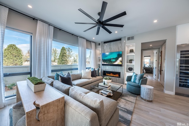 living room featuring light hardwood / wood-style flooring, wine cooler, a tiled fireplace, ceiling fan, and built in features