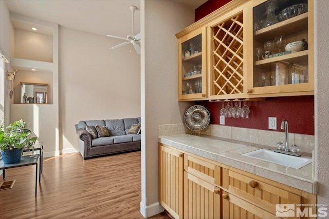 bar with baseboards, a ceiling fan, light wood-style flooring, a sink, and indoor wet bar