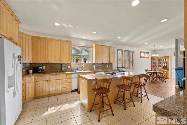 kitchen with light brown cabinetry, white appliances, a breakfast bar, and a center island