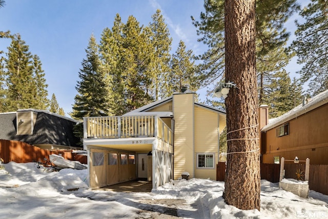 snow covered house featuring a carport and fence