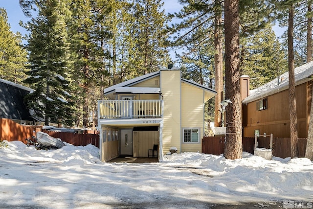 snow covered rear of property with a balcony and fence