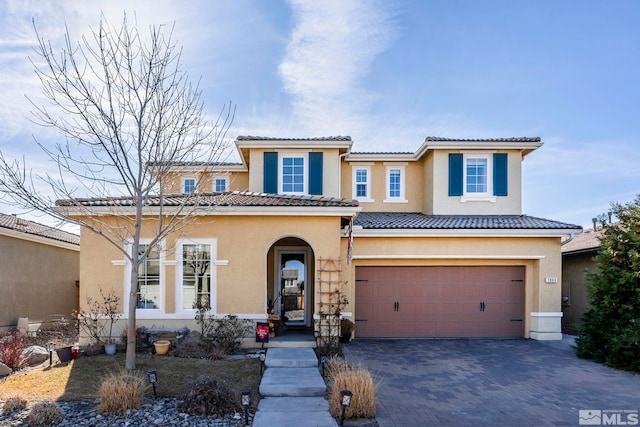 mediterranean / spanish house with decorative driveway, a tile roof, an attached garage, and stucco siding