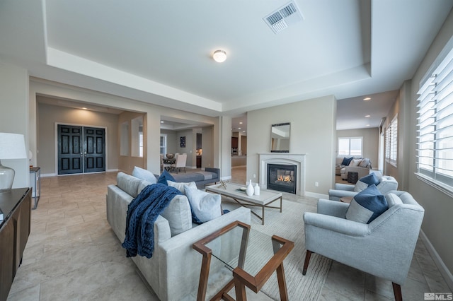 living area with visible vents, a tray ceiling, and a glass covered fireplace