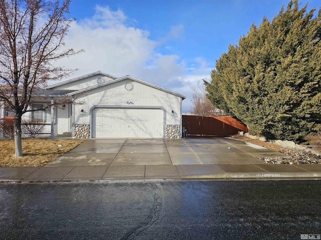 view of side of home featuring a garage, stone siding, driveway, and fence