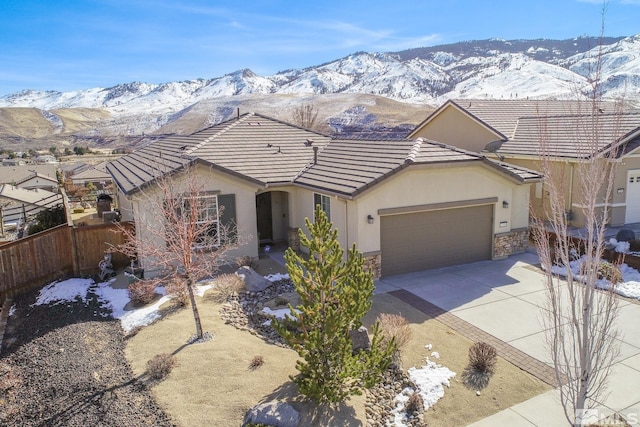 ranch-style house featuring concrete driveway, a mountain view, fence, a garage, and stone siding