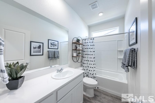 full bathroom with toilet, wood finished floors, vanity, visible vents, and shower / tub combo with curtain