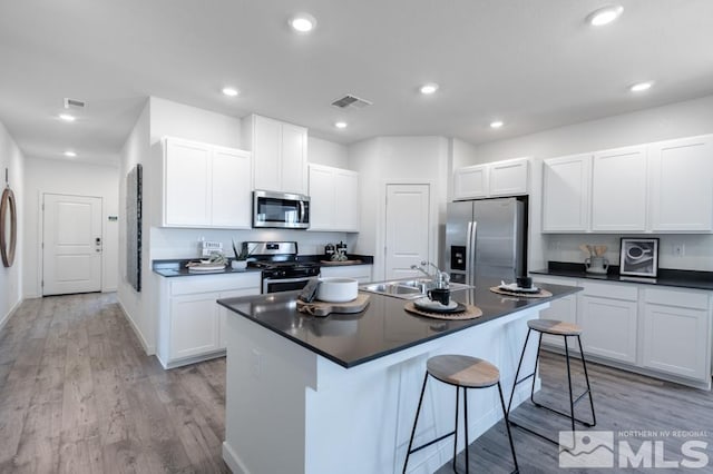 kitchen with a center island with sink, stainless steel appliances, dark countertops, visible vents, and white cabinets