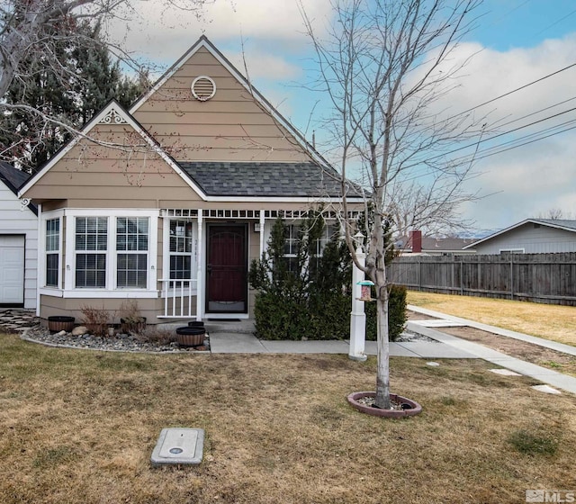 view of front facade featuring a shingled roof, fence, and a front lawn