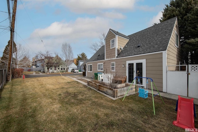 exterior space featuring a shingled roof, fence, a garden, a yard, and a residential view