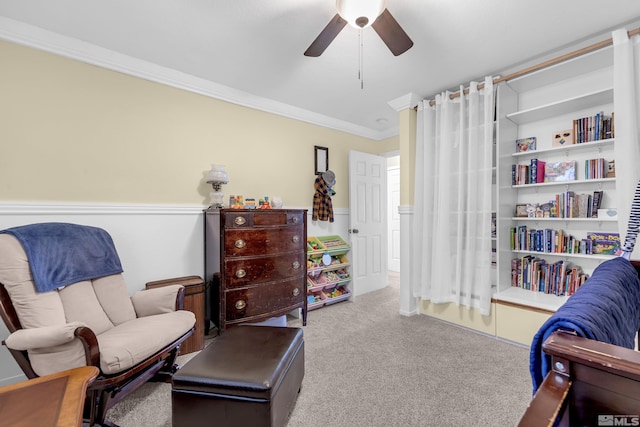 sitting room with ornamental molding, wainscoting, a ceiling fan, and light colored carpet