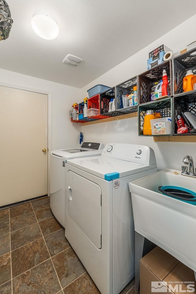 washroom featuring a sink, laundry area, a textured ceiling, and washing machine and dryer