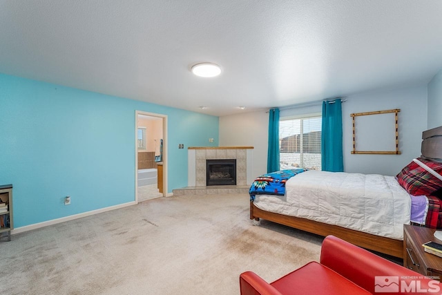 bedroom featuring a textured ceiling, light colored carpet, a fireplace, baseboards, and ensuite bath