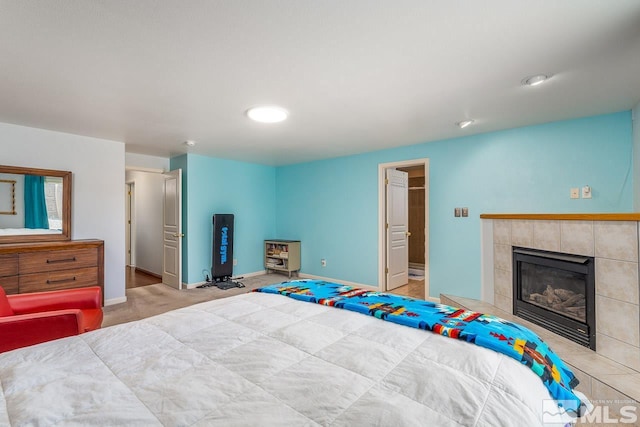 bedroom featuring a tile fireplace, light carpet, and baseboards