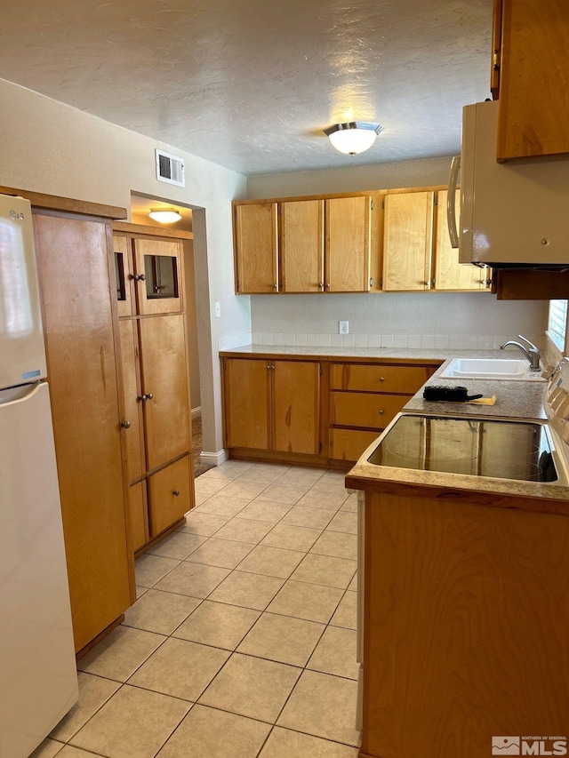 kitchen with visible vents, a sink, white appliances, brown cabinetry, and light tile patterned floors