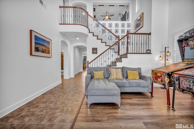 living room with arched walkways, wood finished floors, visible vents, baseboards, and stairway