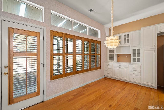 unfurnished dining area with a chandelier, light wood-style flooring, visible vents, baseboards, and wallpapered walls