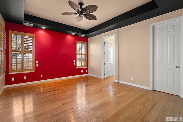 empty room with ceiling fan, an accent wall, visible vents, baseboards, and light wood finished floors