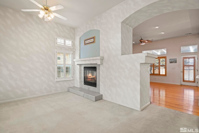 unfurnished living room with a tiled fireplace, a wealth of natural light, and light colored carpet