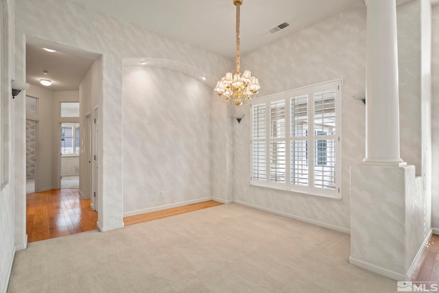 carpeted empty room featuring ornate columns, visible vents, a notable chandelier, and baseboards