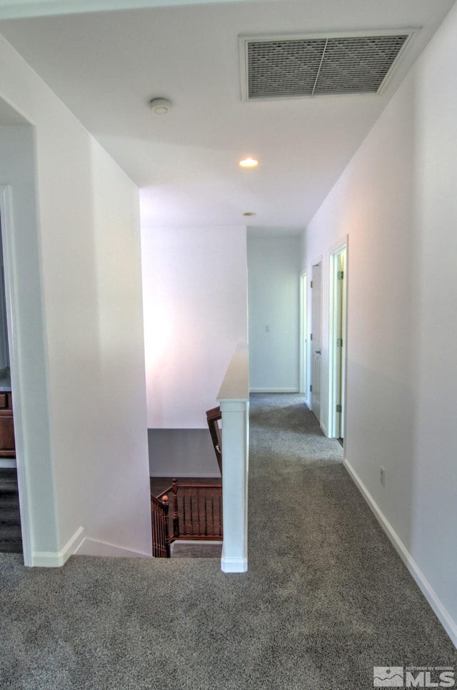 corridor with dark colored carpet, baseboards, visible vents, and an upstairs landing