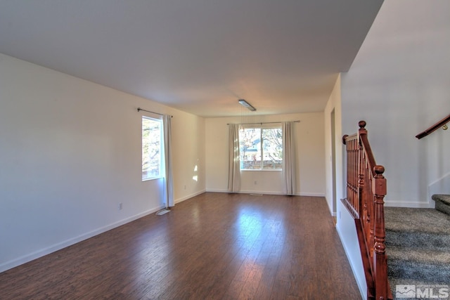 unfurnished living room with a healthy amount of sunlight, stairs, baseboards, and dark wood-type flooring